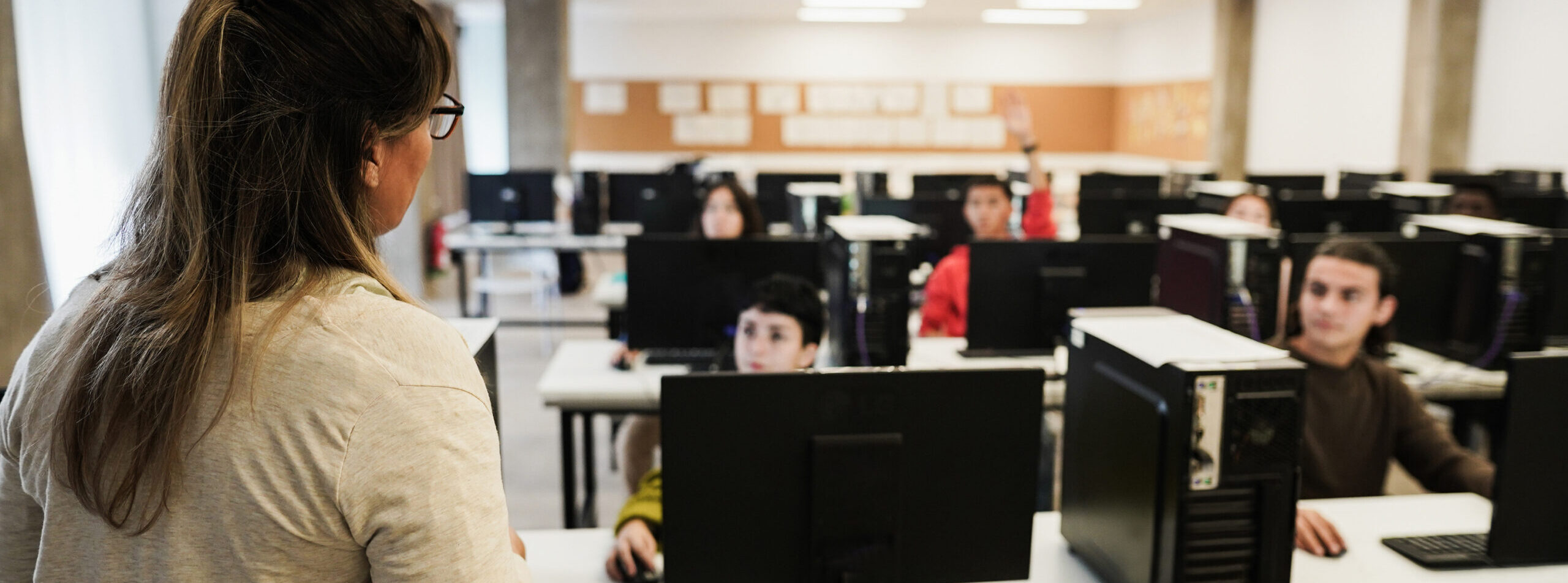 Mature teacher working with students inside computer room at school - Focus on woman shoulder